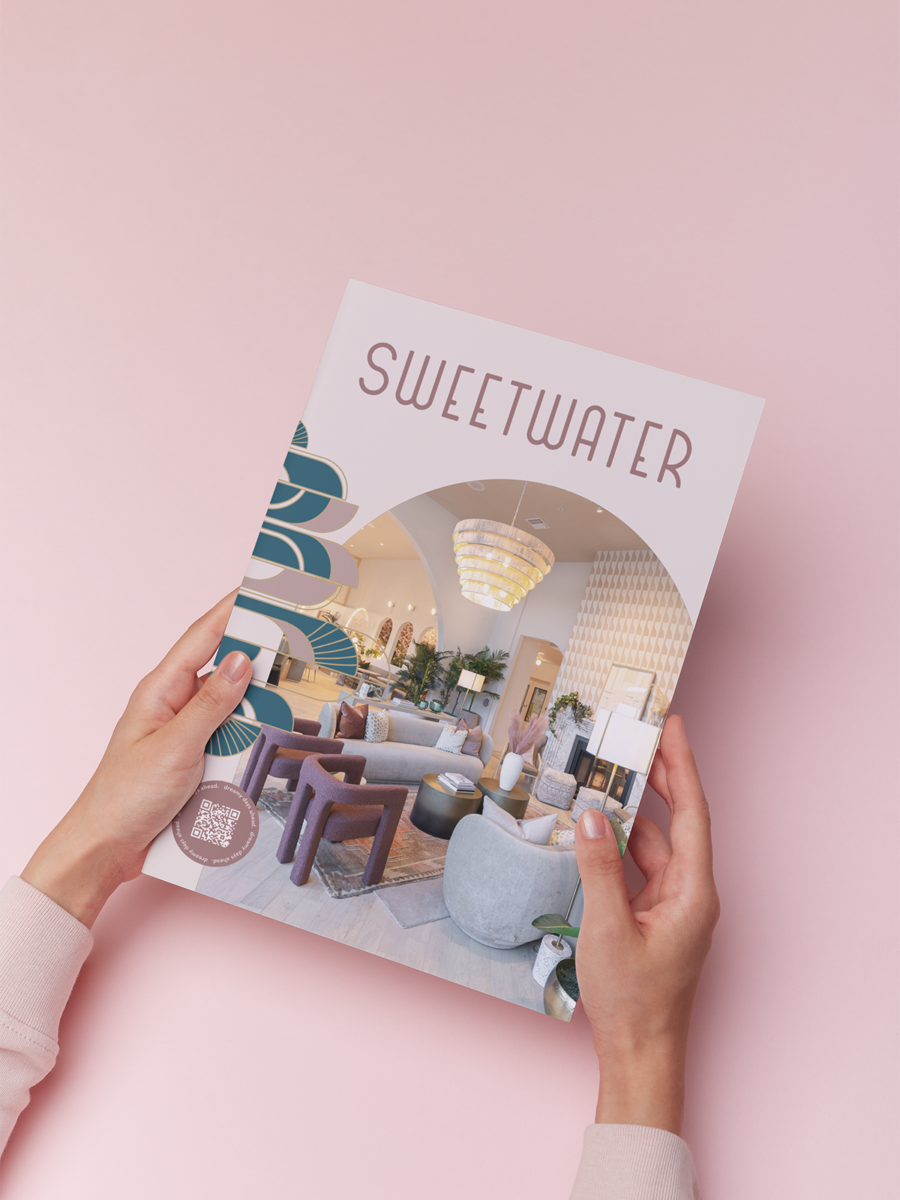 A person holds a magazine with the title SWEETWATER on the cover, featuring a photo of a stylish, modern lounge area with plush seating and a large chandelier, on a pale pink background.