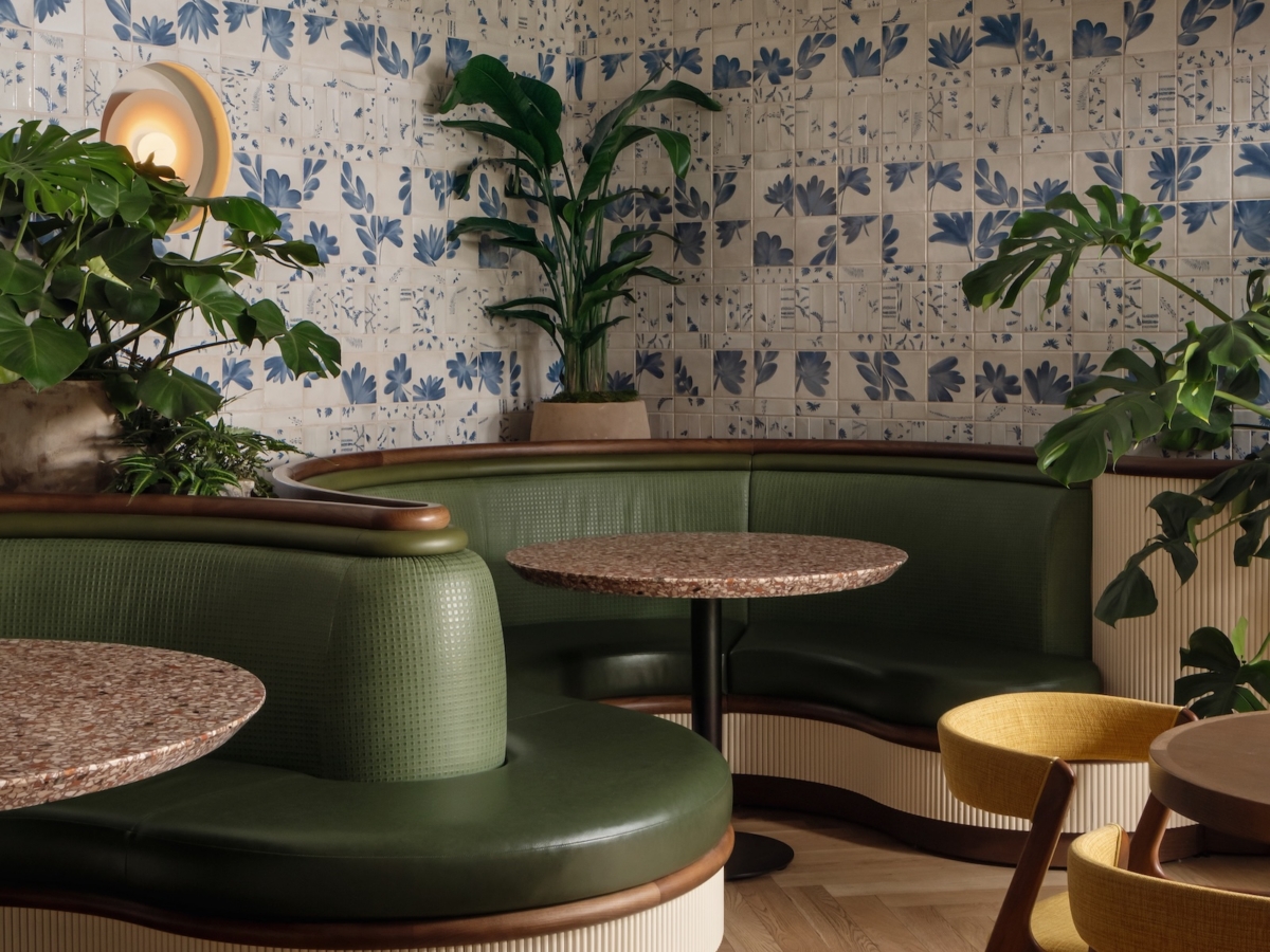Vibrant cafe seating area by Studio 55 featuring green and yellow tables, accented with lush plants.