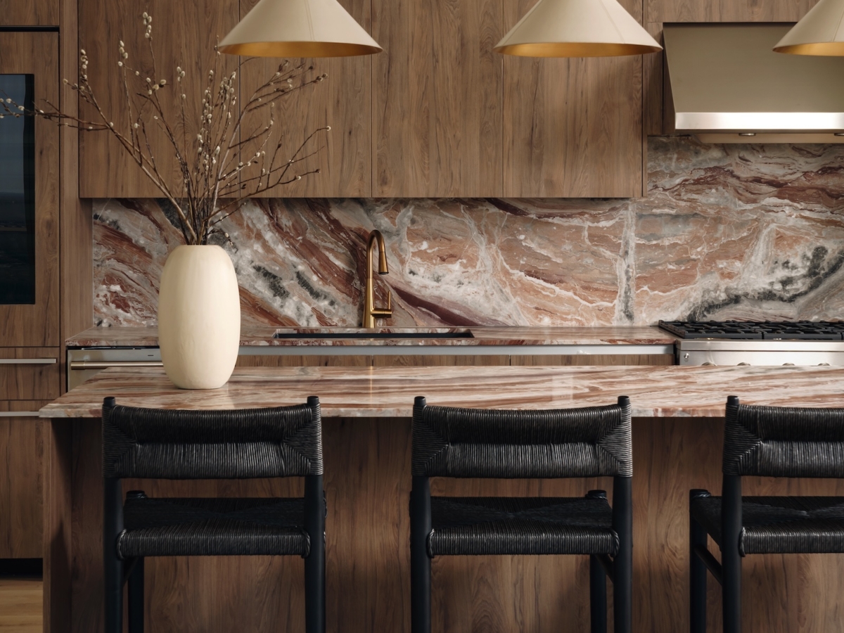 A modern Studio 55 penthouse kitchen features a marble island with three black chairs, wood cabinets, a marble backsplash, gold pendant lights, and a white vase with branches on the counter.